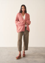 Woman wearing rose pink chunky knit cardigan with soft green trousers and a white blouse
