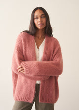 Woman wearing rose pink chunky knit cardigan with soft green trousers and a white blouse