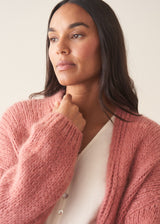 Woman wearing rose pink chunky knit cardigan with soft green trousers and a white blouse