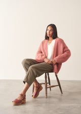 Woman wearing rose pink chunky knit cardigan with soft green trousers and a white blouse