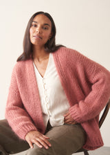 Woman wearing rose pink chunky knit cardigan with soft green trousers and a white blouse