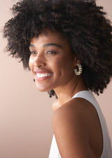 Model wearing chunky gold hoop earrings adorned with crystals, with a white top