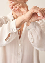 A woman wearing a vintage white long-sleeve button-up sheer blouse and light green khaki trousers.