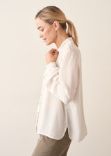 A woman wearing a vintage white long-sleeve button-up sheer blouse and light green khaki trousers.