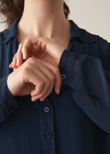 Woman wearing a dark teal blouse and white barrel leg jeans 