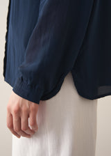 Woman wearing a dark teal blouse and white barrel leg jeans 