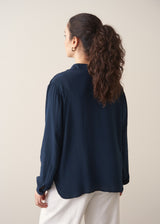 Woman wearing a dark teal blouse and white barrel leg jeans 