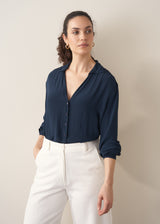 Woman wearing a dark teal blouse and white barrel leg jeans 