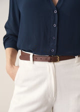 Woman wearing a dark teal blouse and white barrel leg jeans 