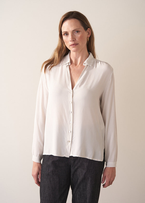 Woman wearing a white silk shirt and dark jeans against a plain background
