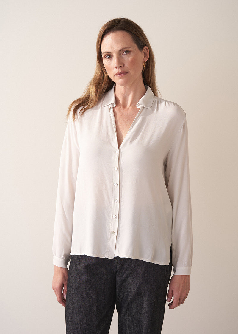 Woman wearing a white silk shirt and dark jeans against a plain background