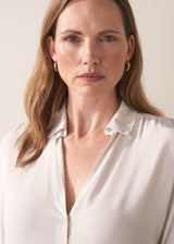 Woman wearing a white silk shirt and dark jeans against a plain background