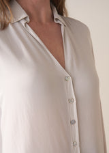 Woman wearing a white silk shirt and dark jeans against a plain background
