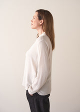 Woman wearing a white silk shirt and dark jeans against a plain background