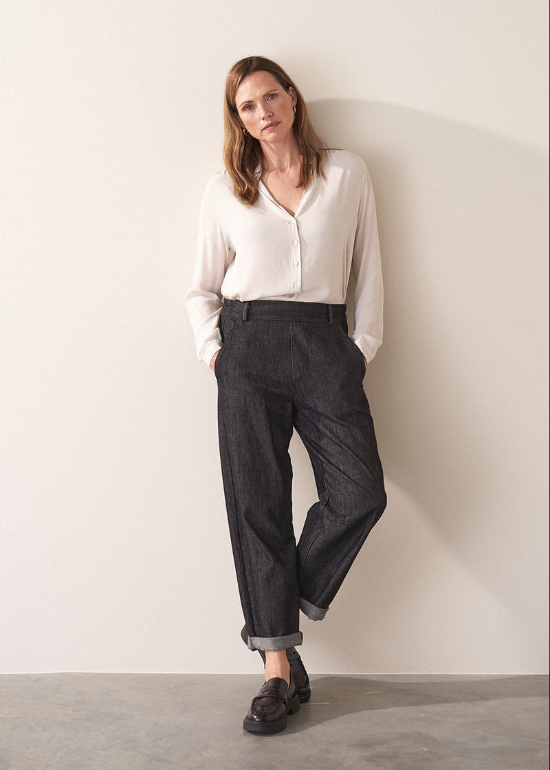 Woman wearing a white silk shirt and dark jeans against a plain background