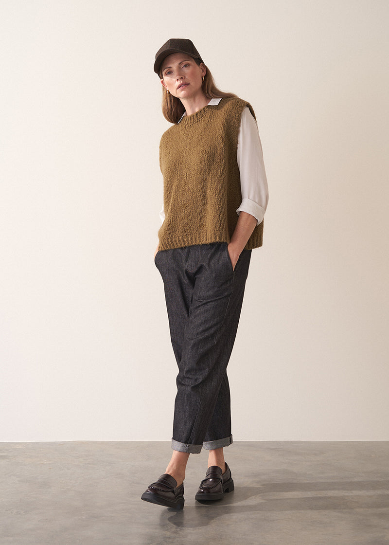 Woman wearing a white silk shirt and dark jeans against a plain background