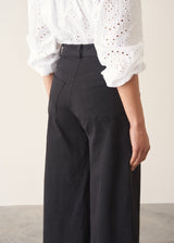 Woman wearing white broderie anglaise top and black cotton wide leg trousers with sandals