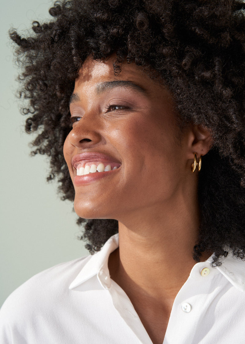 Woman wearing gold double hoop earrings with white shirt