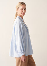 Woman wearing blue pintuck shirt with beige linen trousers