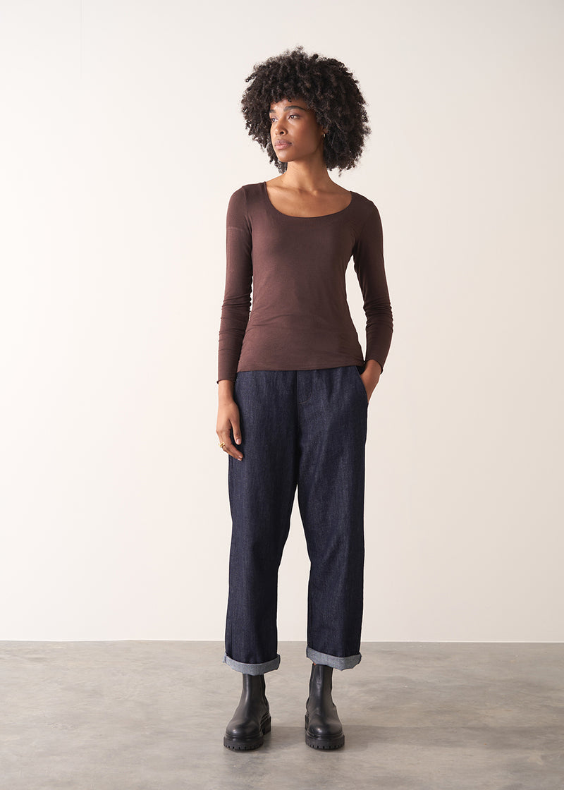 Woman wearing a brown long-sleeve cashmere blend top and blue jeans against a white background