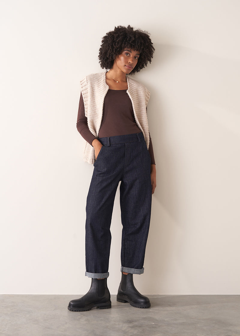 Woman wearing a brown long-sleeve cashmere blend top and blue jeans against a white background