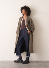 Woman wearing a brown long-sleeve cashmere blend top and blue jeans against a white background