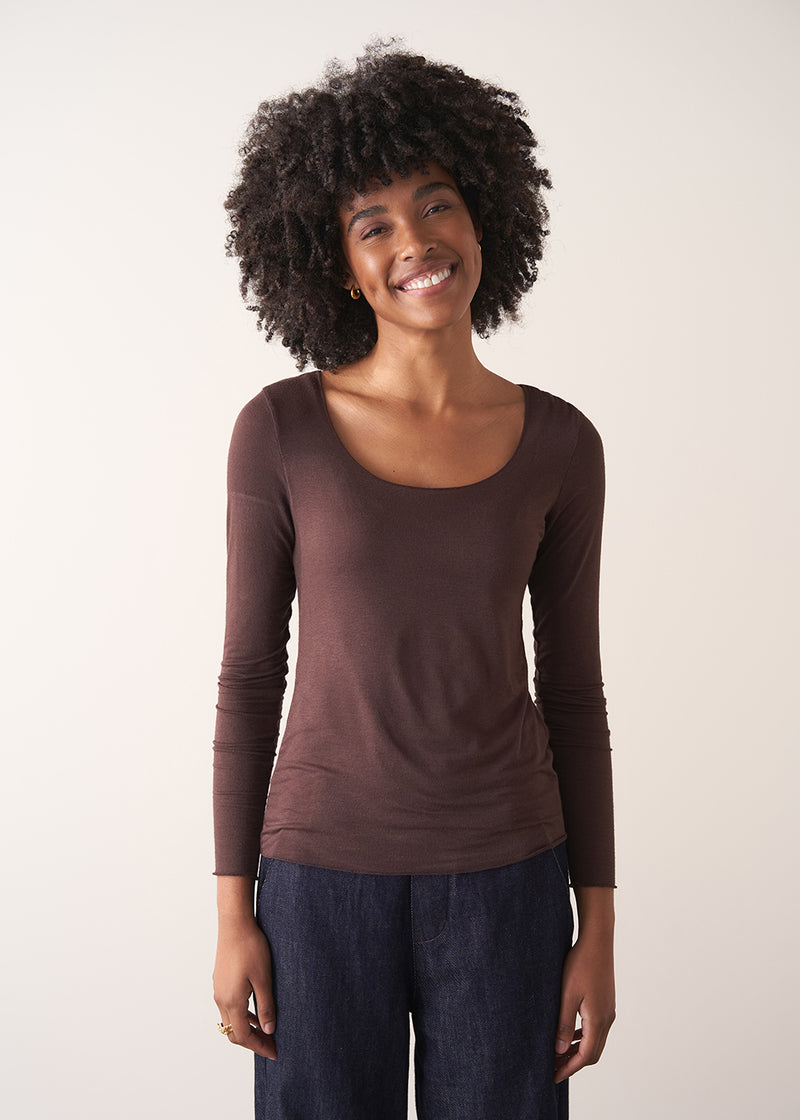 Woman wearing a brown long-sleeve cashmere blend top and blue jeans against a white background