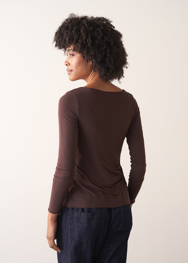 Woman wearing a brown long-sleeve cashmere blend top and blue jeans against a white background