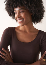 Woman wearing a brown long-sleeve cashmere blend top and blue jeans against a white background