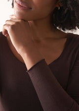 Woman wearing a brown long-sleeve cashmere blend top and blue jeans against a white background