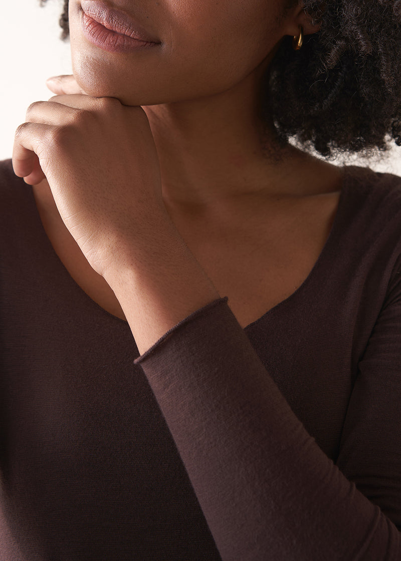 Woman wearing a brown long-sleeve cashmere blend top and blue jeans against a white background