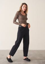 A woman wearing a form fitting long sleeve leopard print top with a grey cardigan and black trousers