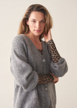 A woman wearing a form fitting long sleeve leopard print top with a grey cardigan and black trousers