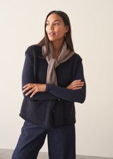 A woman wearing a dark blue long sleeve cashmere blend layering top with dark blue jeans and stud loafers. 