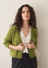 Woman wearing a green marled v-neck cardigan with a white top and black trousers