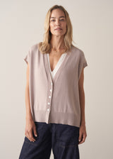 Woman wearing a beige sleeveless button up cardigan with blue jeans 