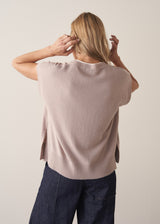 Woman wearing a beige sleeveless button up cardigan with blue jeans 