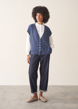 Woman wearing a blue knitted waistcoat, white embroidered top and denim jeans. 