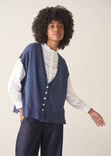 Woman wearing a blue knitted waistcoat, white embroidered top and denim jeans. 