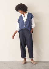 Woman wearing a blue knitted waistcoat, white embroidered top and denim jeans. 