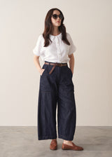 Woman wearing a white shirt and dark blue denim cargo trousers against a plain background