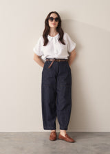 Woman wearing a white shirt and dark blue denim cargo trousers against a plain background