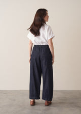 Woman wearing a white shirt and dark blue denim cargo trousers against a plain background