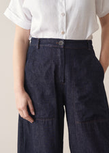 Woman wearing a white shirt and dark blue denim cargo trousers against a plain background
