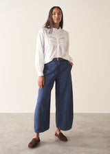 A woman wearing a white long-sleeve embroidered blouse and blue wide-leg cargo trousers, paired with brown loafers.
