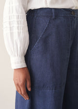 A woman wearing a white long-sleeve embroidered blouse and blue wide-leg cargo trousers, paired with brown loafers.