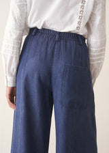 A woman wearing a white long-sleeve embroidered blouse and blue wide-leg cargo trousers, paired with brown loafers.