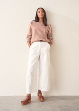 Woman wearing white denim barrel leg trousers with a burnt orange stripe knit sweater and brown belt.