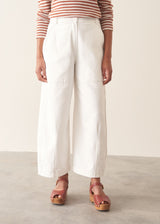Woman wearing white denim barrel leg trousers with a burnt orange stripe knit sweater and brown belt.