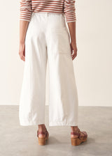 Woman wearing white denim barrel leg trousers with a burnt orange stripe knit sweater and brown belt.
